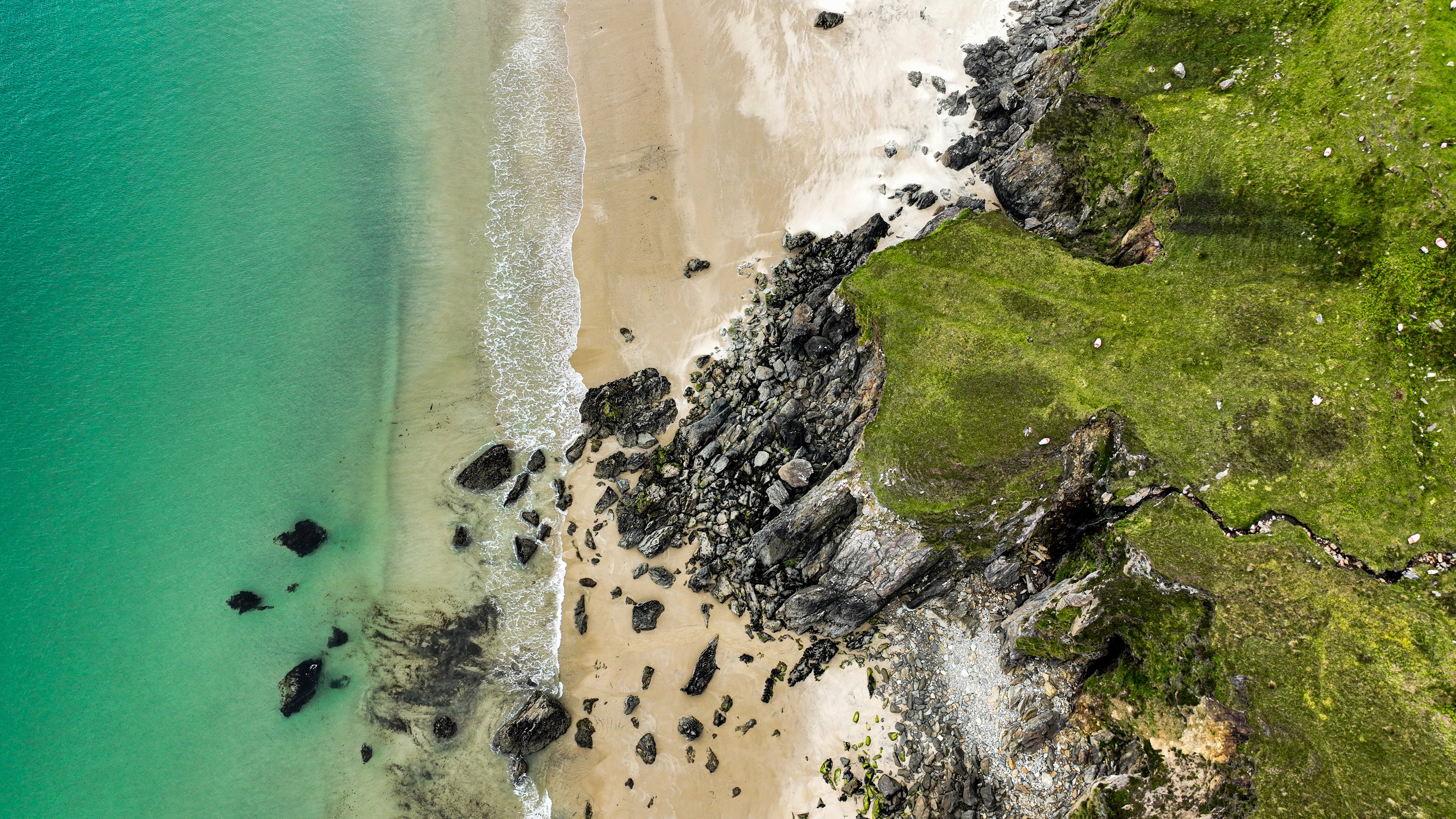 Aerial view of a beach with turquoise water and green algae-covered rocks.