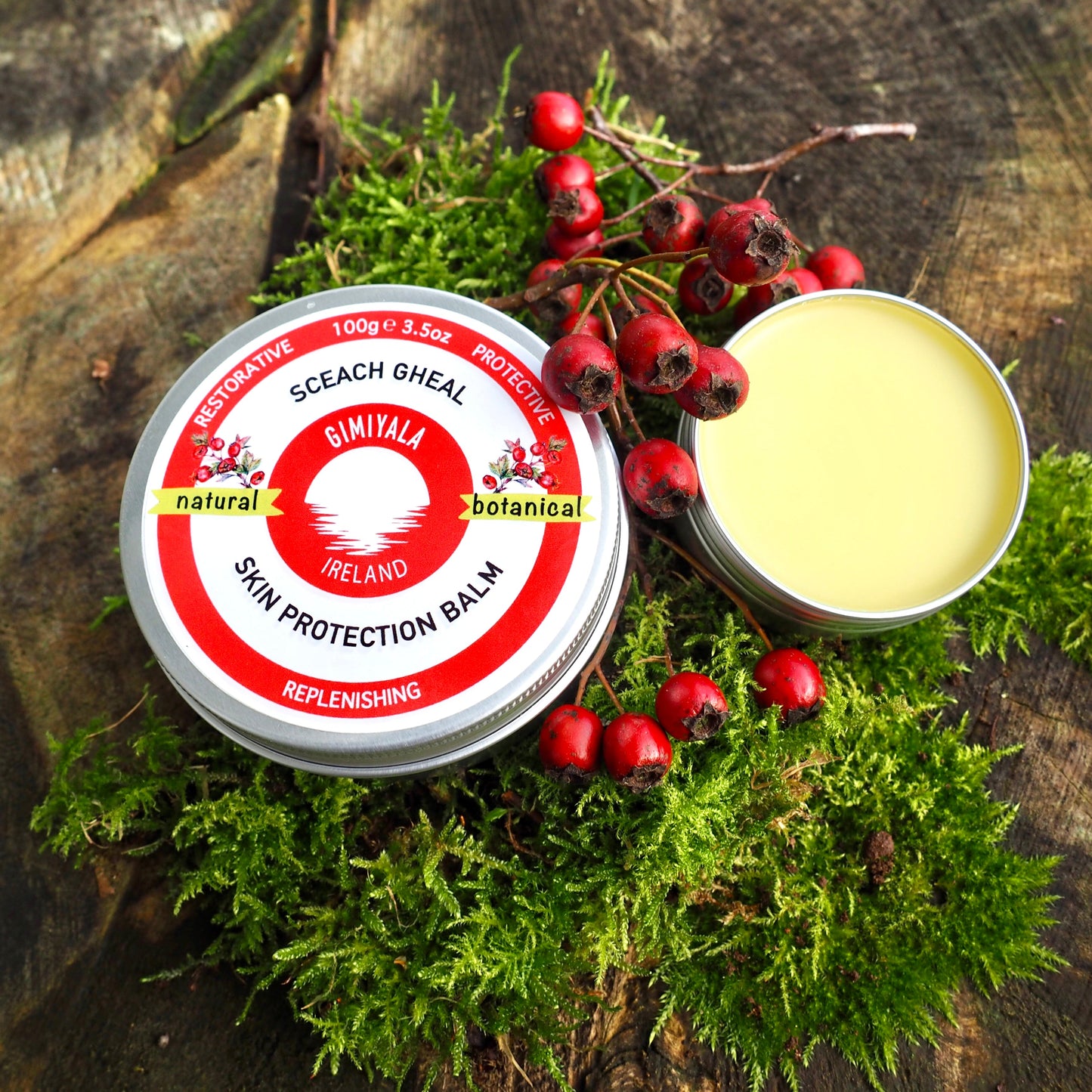 Balm tin with red label on a wooden surface with green moss and red berries